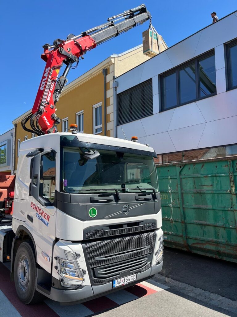 LKW-Kran hebt Kiste auf Gebäude.